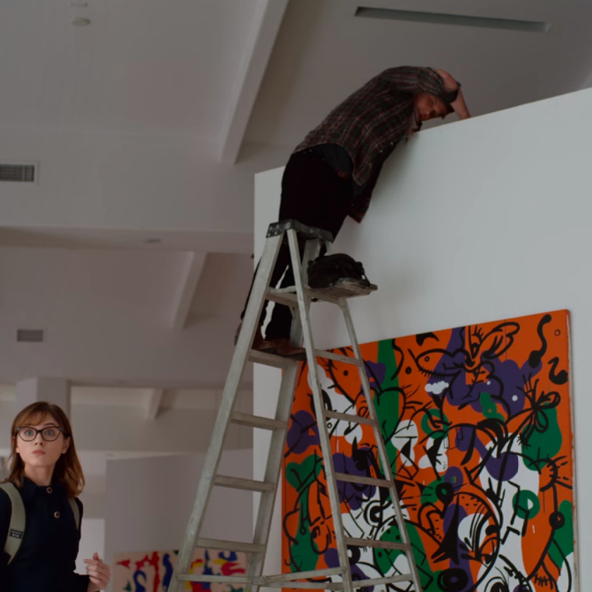image from 'Velvet Buzzsaw' (2019) of art installer on top of ladder above piece of artwork
